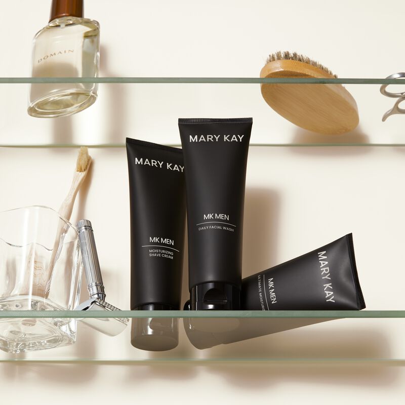 MKMen Moisturizing Shave Cream, MKMen Daily Facial Wash and MKMen Ultimate Moisturizer on a shelf next to a razor, men&rsquo;s brush and other toiletries.