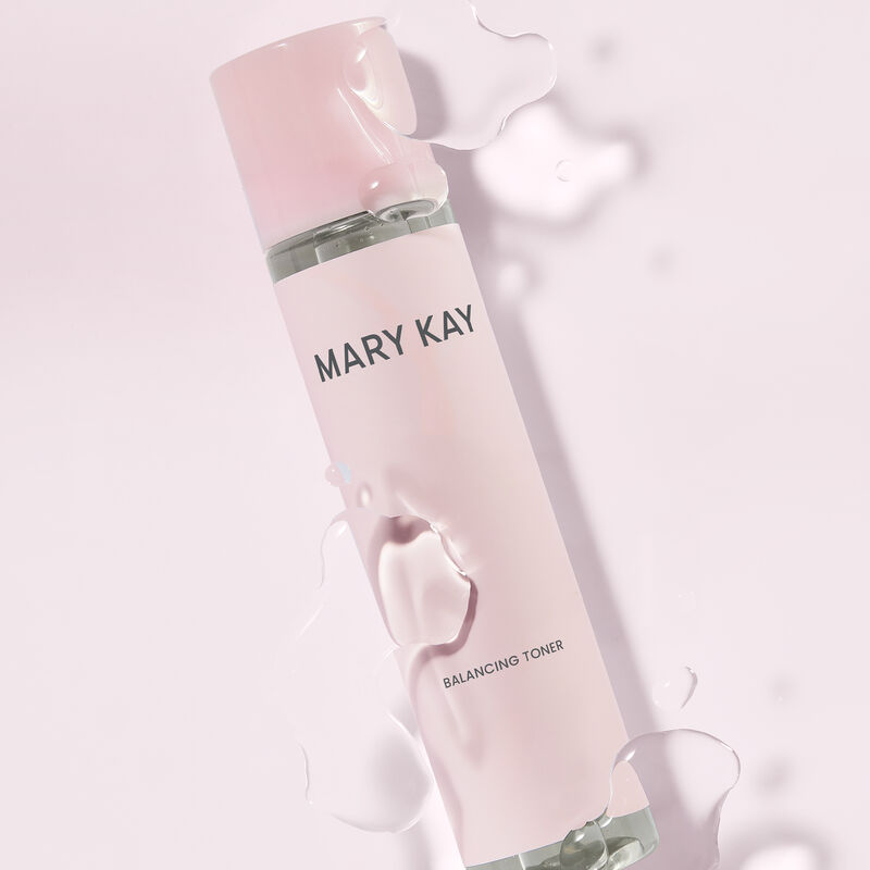 Bouteille du Tonique &eacute;quilibrant Mary Kay sous des gouttes du produit sur un fond rose p&acirc;le
