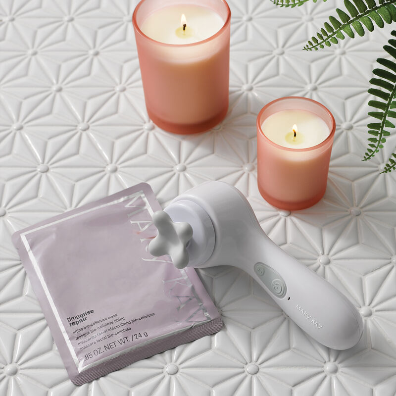 Packet of TimeWise Repair Lifting Bio-Cellulose Mask from Mary Kay styled with Skinvigorate Sonic Skin Care System, candles and a plant.