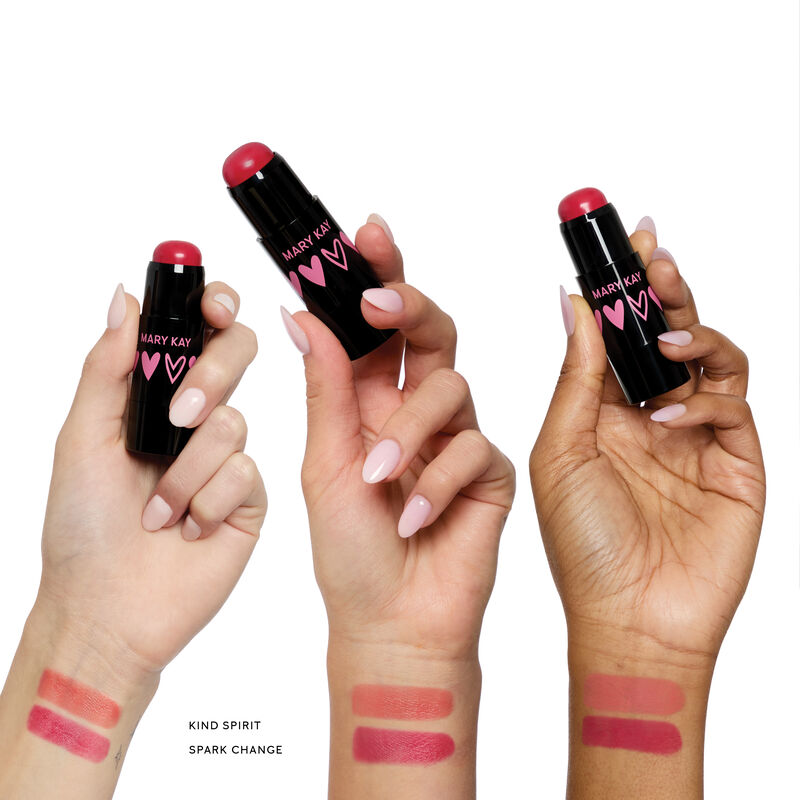 Three hands holding limited-edition Mary Kay Blush Stick in Kind Spirit shade, showing swatches of two shades on different skin tones.