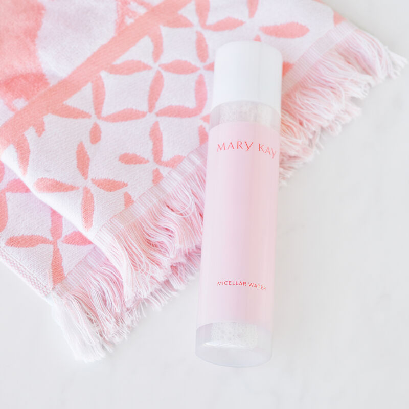 Bottle of Mary Kay Micellar Water laying on a pink and white patterned hand towel on white countertop