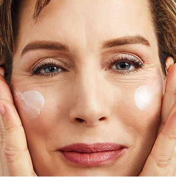 Femme souriant &agrave; la cam&eacute;ra en train d&rsquo;appliquer le S&eacute;rum r&eacute;g&eacute;n&eacute;rateur C+E TimeWise Mary Kay sur ses joues