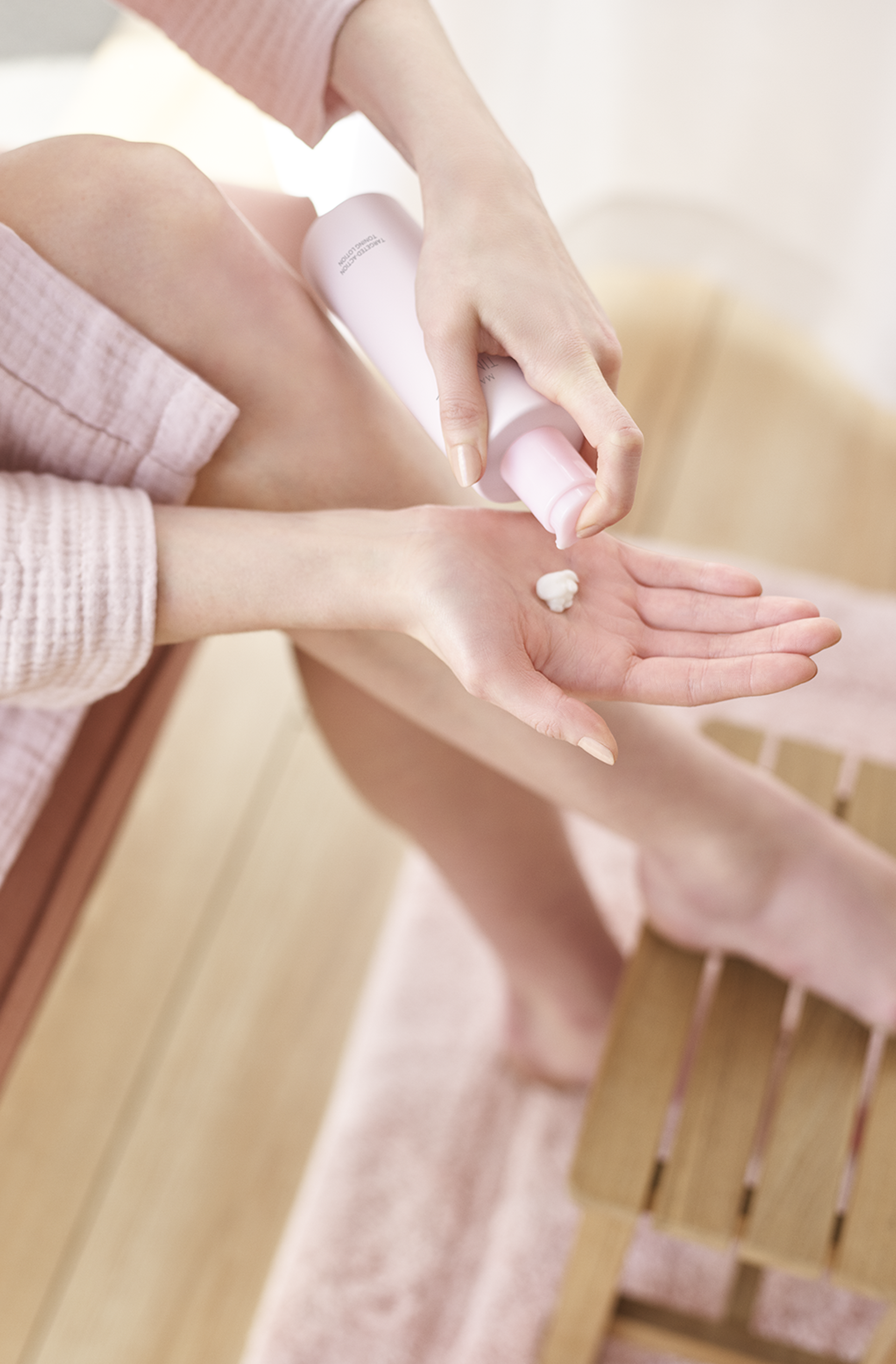 A person seated on a wooden bench dispenses a dollop of Mary Kay Toning Lotion into their palm.