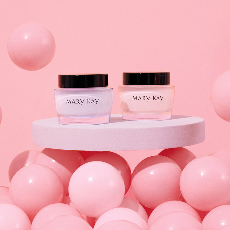 Un pot de Gel hydratant sans huile Mary Kay et un pot de Cr&egrave;me hydratante intense Mary Kay sont dispos&eacute;s sur une table blanche entour&eacute;e de ballons roses. 