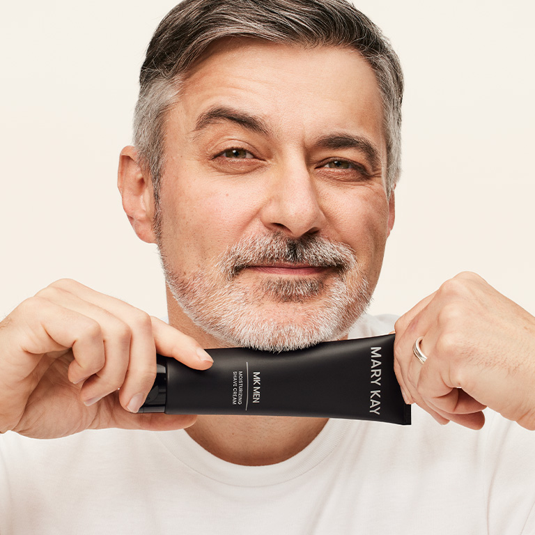 Un homme souriant, tenant un tube de cr&egrave;me &agrave; raser Mary Kay MKMen contre son menton