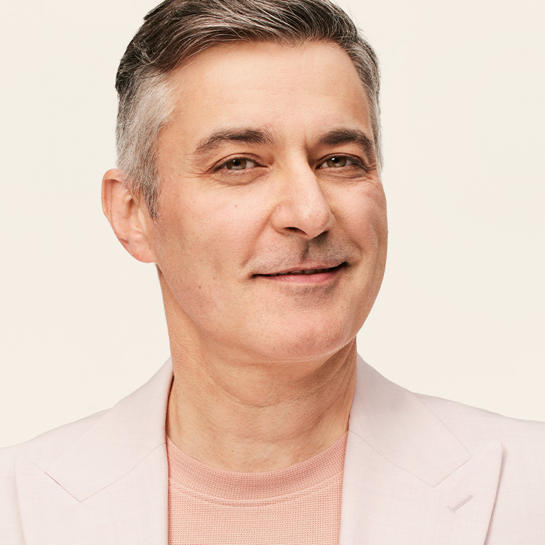 Une personne qui vient de se raser, portant un blazer rose p&acirc;le sur un haut de couleur neutre, devant un fond beige uni.