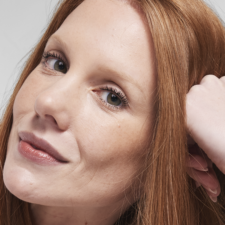 Une mannequin rousse regarde l'objectif, le teint rehauss&eacute; par le fond de teint Luminous au fini &eacute;clatant.